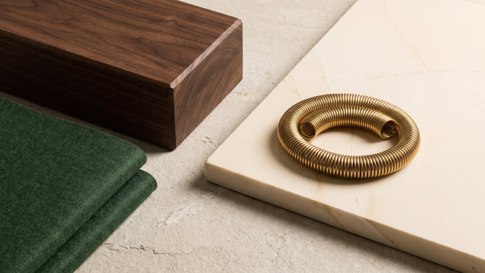 A dark wood block, a folded piece of green felt, and a coiled brass spring are arranged on split planes of light-colored stone.