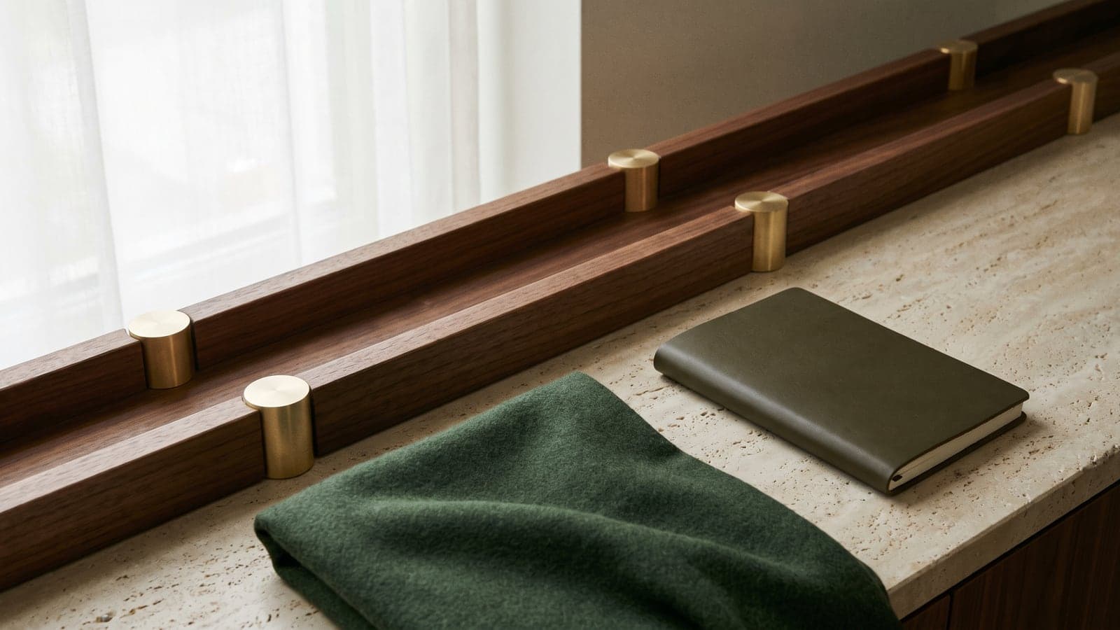Parallel walnut rails with brass fittings rest on a limestone surface next to a green cloth and notebook in soft light.