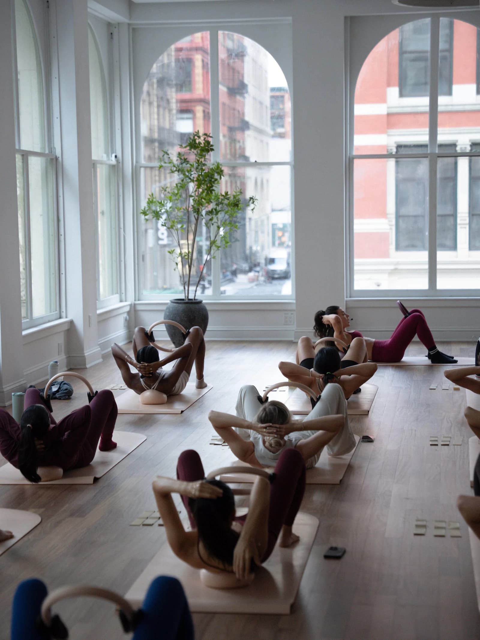 Participants practicing on mats with Pilates rings beside tall arched windows