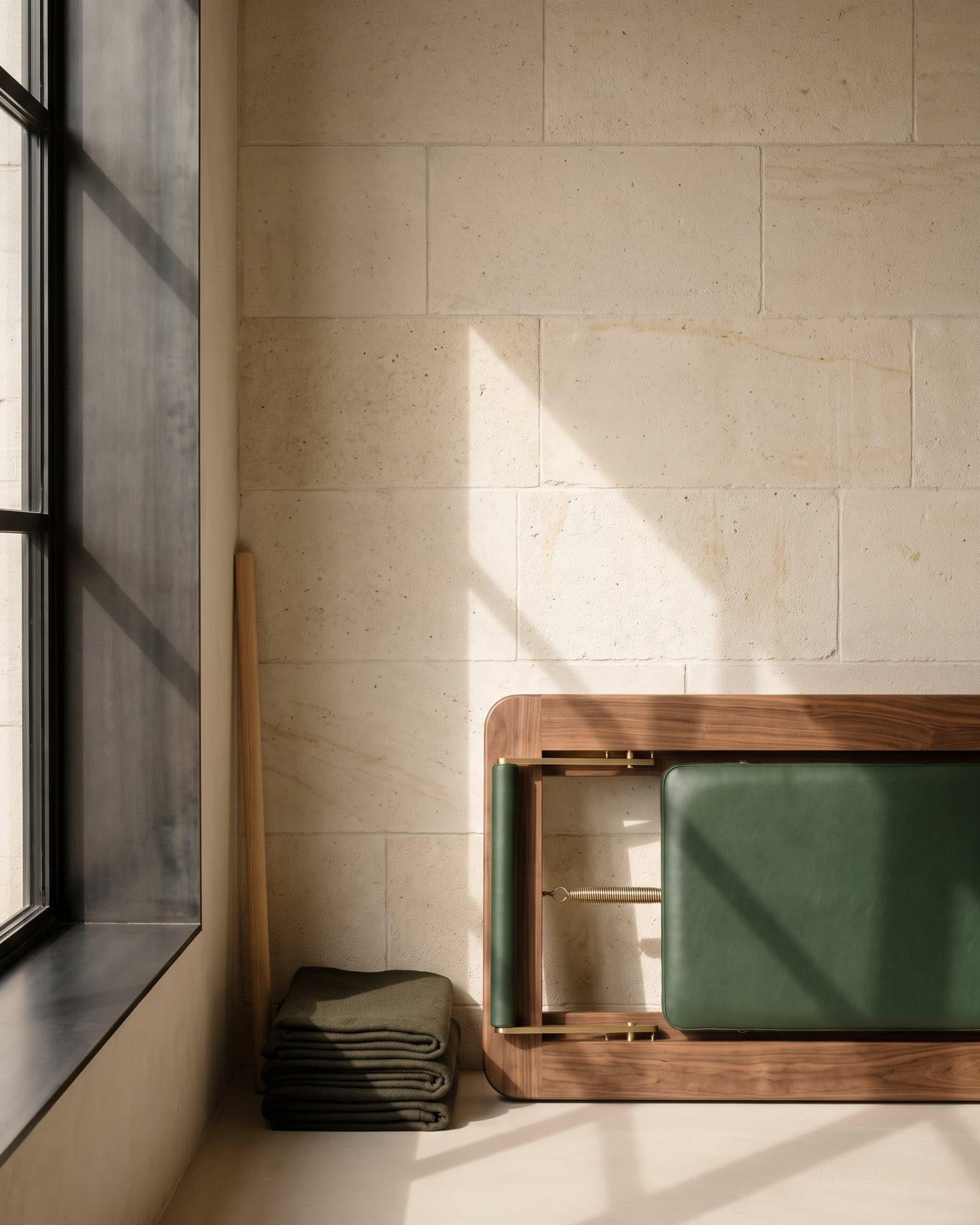 Limestone grid, dark metal threshold, and walnut edge crossed by window light