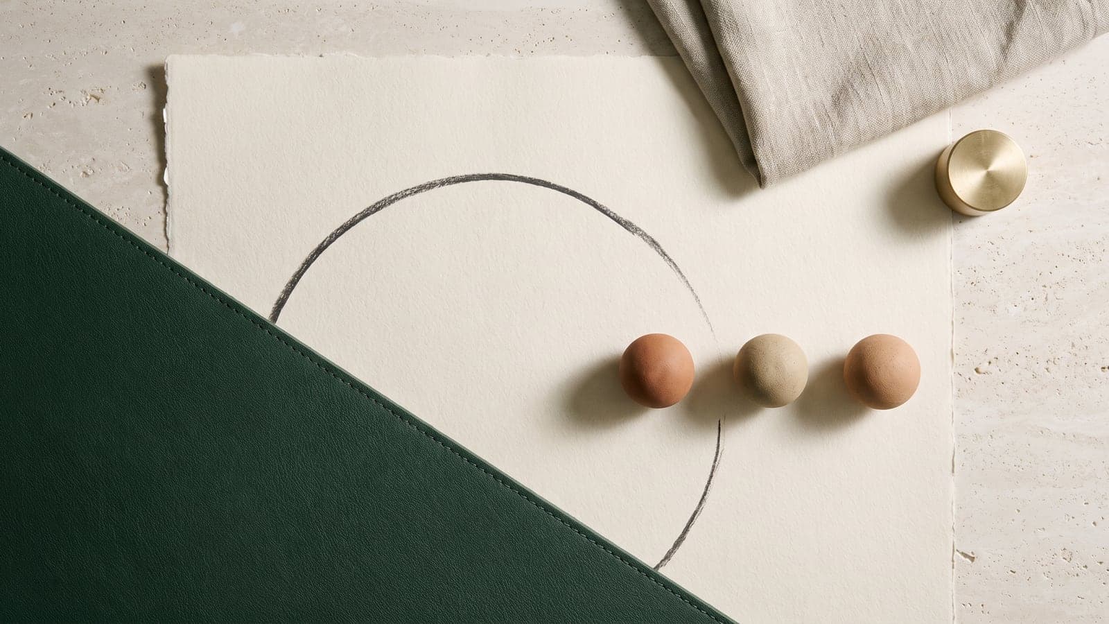Forest green mat edge, charcoal arc, and three clay spheres spaced across pale limestone